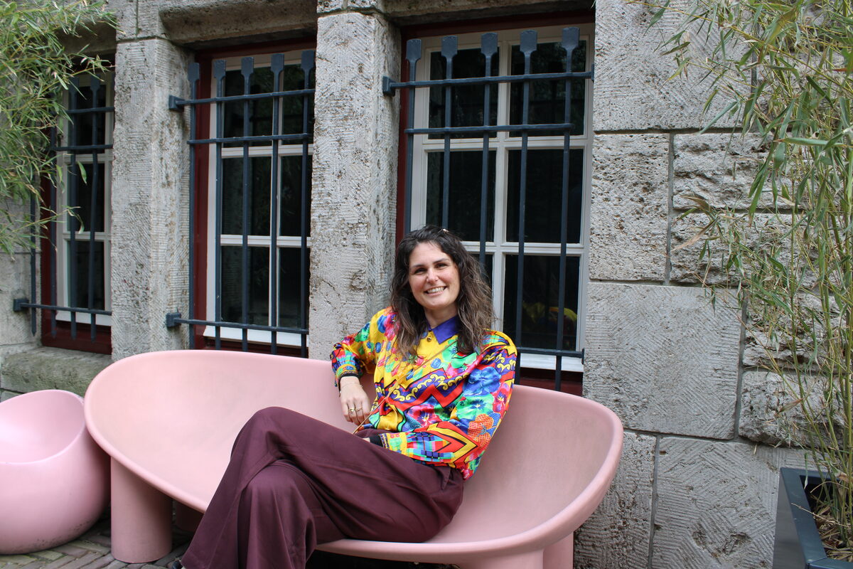 Gabriëlle sitting on a bench outside in front of a museum in a colourful blouse